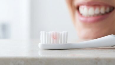 A macro photo showing a toothbrush with a faint red tint on its bristles, indicating an early sign of gum disease, with a person's healthy mouth blurred in the background.