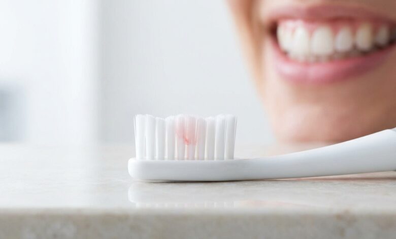 A macro photo showing a toothbrush with a faint red tint on its bristles, indicating an early sign of gum disease, with a person's healthy mouth blurred in the background.