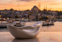 An abstract white shape resembling a perfect smile in the foreground, with a blurred, warm-toned background of the Istanbul, Turkey skyline at sunset, representing a dental holiday.