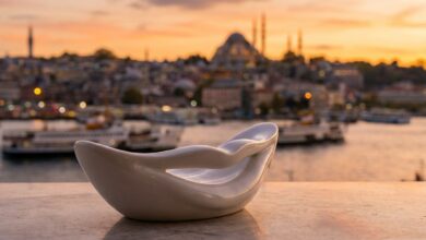 An abstract white shape resembling a perfect smile in the foreground, with a blurred, warm-toned background of the Istanbul, Turkey skyline at sunset, representing a dental holiday.