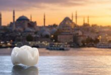 A photorealistic close-up of a single, perfect dental implant crown on a clean surface, with the beautiful, blurred skyline of Istanbul, Turkey, during sunrise in the background, symbolizing a dental tourism holiday.