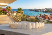 A close-up, photorealistic shot of a perfect set of white porcelain dental veneers, with a beautifully blurred background showing a sunny, coastal city in Turkey. The scene represents the concept of dental tourism.