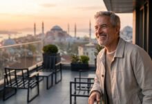 A mature man with a brilliant, healthy smile stands on a balcony with a scenic, blurred background of Istanbul, Turkey at sunrise. The image conveys a sense of happiness and satisfaction after a successful dental treatment abroad.