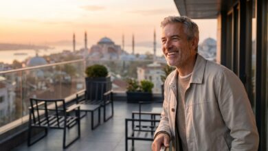 A mature man with a brilliant, healthy smile stands on a balcony with a scenic, blurred background of Istanbul, Turkey at sunrise. The image conveys a sense of happiness and satisfaction after a successful dental treatment abroad.