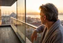 A person viewed from behind, looking out from a modern balcony at a softly blurred, golden sunrise over the Istanbul, Turkey skyline, symbolizing a successful and safe dental tourism trip.