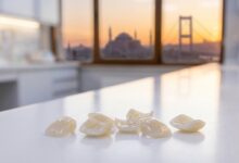 A photorealistic close-up of pristine white dental veneers on a clean surface, with the blurred skyline of Istanbul, Turkey and the Bosphorus visible in the background during a warm sunset.