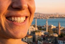 Close-up of a person's flawless, white smile, with a beautiful, sunlit, and blurred Turkish city coastline in the background, representing a successful dental tourism trip.