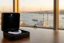 A close-up of a perfect set of white dental veneers in a display case. In the background, the Istanbul skyline and the Bosphorus are visible in a beautiful, blurred sunset, symbolizing dental tourism in Turkey.