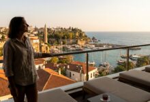 A photorealistic image from a high-rise balcony showing a person with a happy smile looking out over a beautiful Turkish coastal city at sunset, symbolizing a successful dental tourism trip.