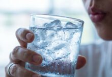 A close-up photo of a person about to drink from a glass of ice water, illustrating the concept of tooth sensitivity and pain from cold drinks.