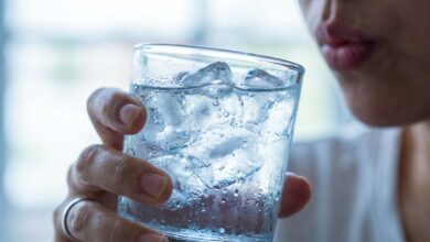 A close-up photo of a person about to drink from a glass of ice water, illustrating the concept of tooth sensitivity and pain from cold drinks.