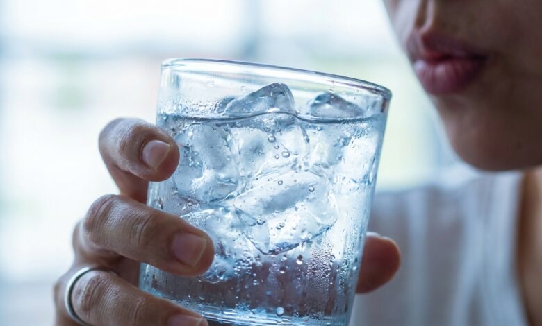 A close-up photo of a person about to drink from a glass of ice water, illustrating the concept of tooth sensitivity and pain from cold drinks.