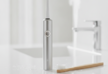 A side-by-side comparison of an electric toothbrush and a manual toothbrush on a clean bathroom counter, highlighting their design differences. The electric toothbrush is modern and sleek, while the manual toothbrush is traditional. The background is blurred, focusing on the two main subjects.