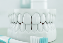 Close-up of perfectly clean, white, healthy teeth in a bright, hygienic setting. A blurred soft-bristled toothbrush and dental floss are visible in the background.