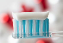 Close-up of a soft-bristled toothbrush with a white ribbon of toothpaste on it, suggesting specialized care for sensitive teeth. The background is a clean, blurred bathroom scene with a subtle red and white color hint in the bokeh, representing Canada.