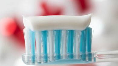 Close-up of a soft-bristled toothbrush with a white ribbon of toothpaste on it, suggesting specialized care for sensitive teeth. The background is a clean, blurred bathroom scene with a subtle red and white color hint in the bokeh, representing Canada.