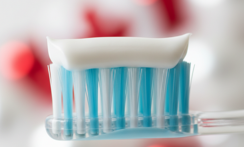Close-up of a soft-bristled toothbrush with a white ribbon of toothpaste on it, suggesting specialized care for sensitive teeth. The background is a clean, blurred bathroom scene with a subtle red and white color hint in the bokeh, representing Canada.