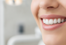 A close-up, photorealistic image of a person's lower face, focusing on a healthy, confident smile with perfectly aligned, naturally white teeth. The background is a softly blurred, clean, and modern dental office environment, conveying professionalism and advanced care. There is no text visible in the image.