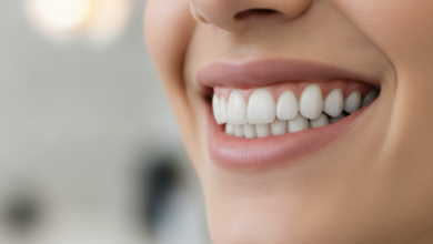 Close-up of a person smiling broadly, showing a full set of healthy, natural-looking, perfectly aligned teeth. The background is a soft, out-of-focus blur of a clean, modern dental office, conveying professionalism and successful dental restoration.