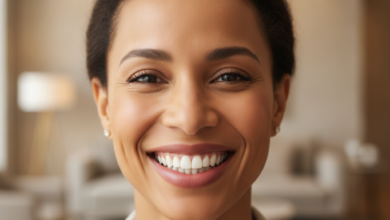 A close-up, photorealistic image of a diverse woman in her 30s genuinely smiling with naturally bright, perfectly aligned teeth, radiating confidence and happiness. The background is softly blurred, showing a warm, inviting modern interior, without any visible text.